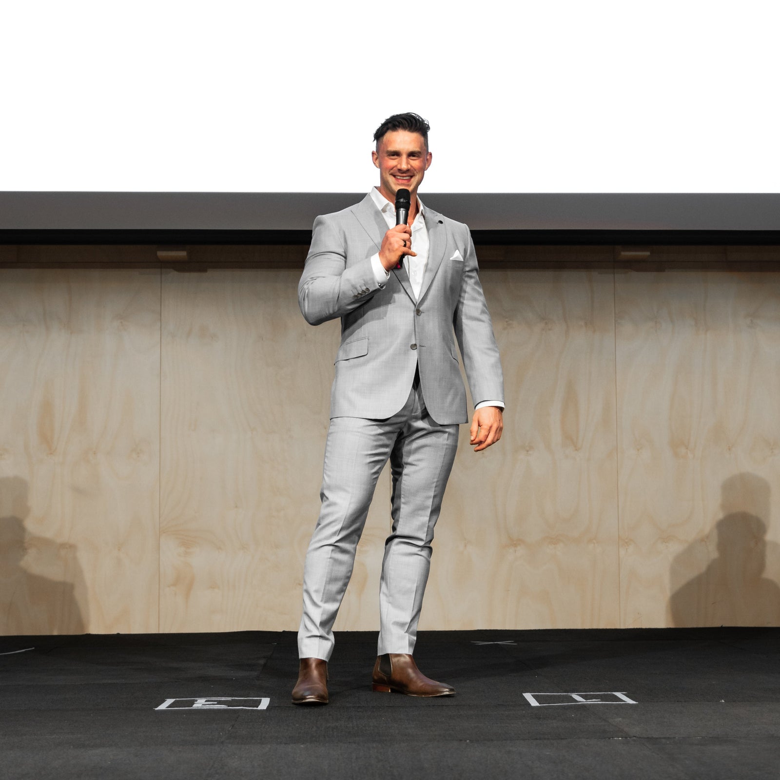 Man in a gray suit standing on a stage with a white background