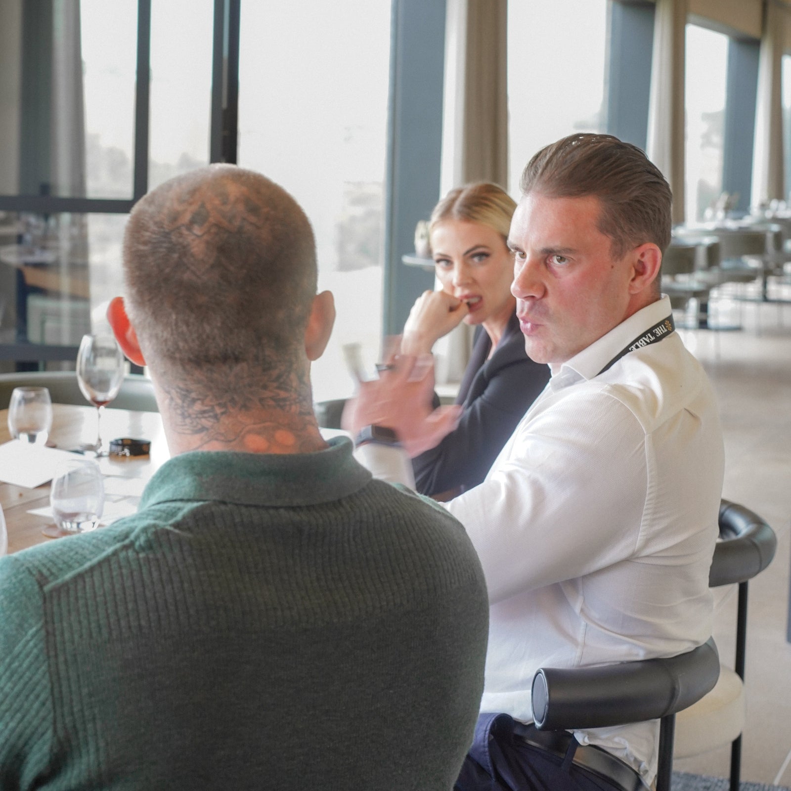 Three people sitting at a table in a modern indoor setting with large windows.